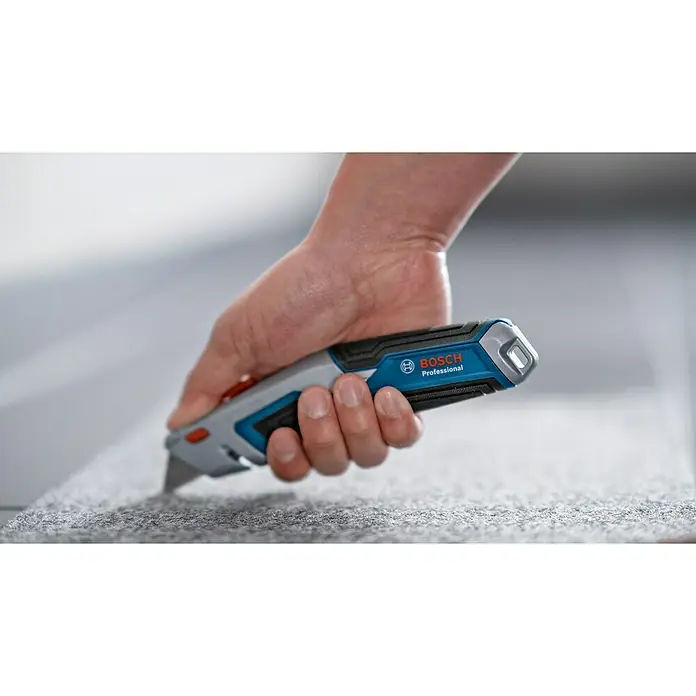 Bosch Professional Cuttermesser - 4 -tlg., Trapezklinge - Nahaufnahme eines Bosch Professional Universalmesser beim Schneiden eines Teppichs.