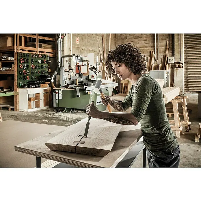 Halder Supercraft Schonhammer - Durchmesser Kopf: 32 mm, Holz - Eine Frau mit Tätowierungen arbeitet mit einem Stecheisen und einem Hammer an einem Holzstück in einer Werkstatt.