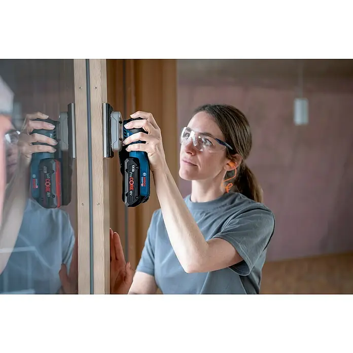 Bosch Professional AMPShare 18V Akku-Schwingschleifer GSS 18V-13 - 18 V, Ohne Akku, Leerlaufschwingzahl: 12.000 U/min - 20.000 U/min - Frau benutzt einen Bosch Akku-Multischleifer zum Schleifen eines Holzrahmens, mit Schutzbrille und Ohrstöpseln.