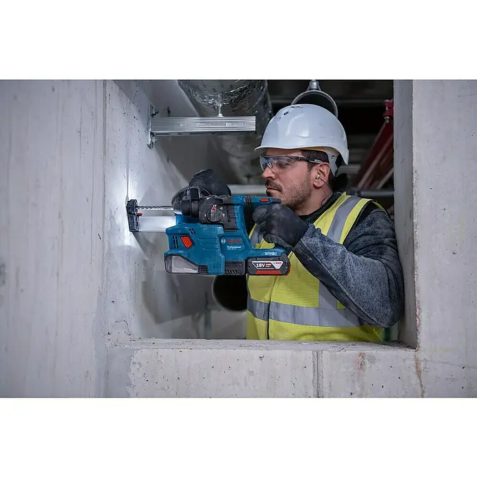 Bosch Professional Staubabsaugung GDE 18V-12 - Passend für: Bosch Professional Bohrhammer GBH 18V-22 - Ein Bauarbeiter bohrt mit einem Bosch Akku-Bohrhammer ein Loch in eine Betonwand. Der Bohrhammer ist blau und hat einen 18V Akku.