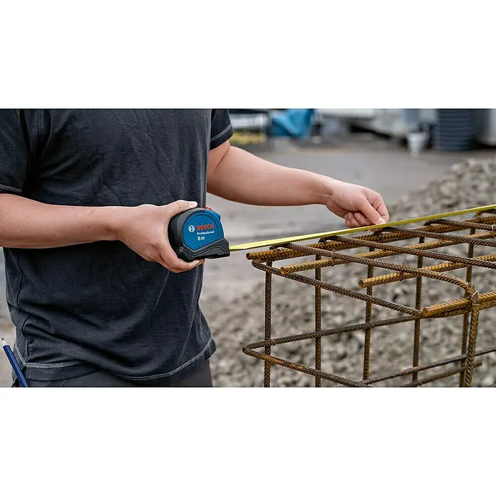 Bosch Professional Kapselmaßband Autolock8 m - Ein Arbeiter misst mit einem Bosch Professional 8m Rollbandmaß ein Bewehrungseisen. Das Maßband ist blau und schwarz, gut erkennbar.