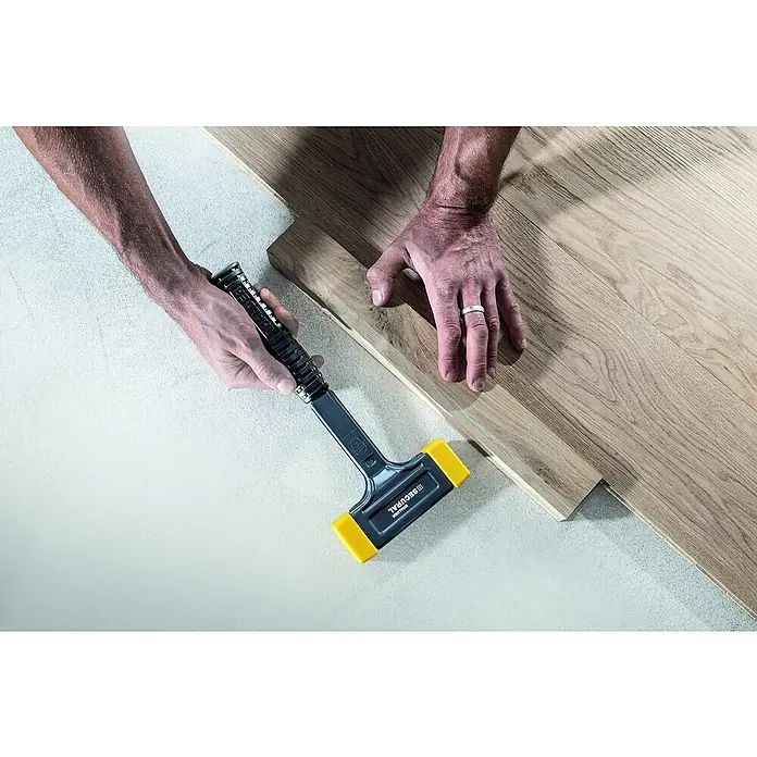 Halder Secural Schonhammer - Stahl, Durchmesser Kopf: 30 mm - Blick auf einen Mann, der mit einem Secural-Hammer einen Holzboden verlegt. Das Werkzeug ist schwarz mit gelben Enden.
