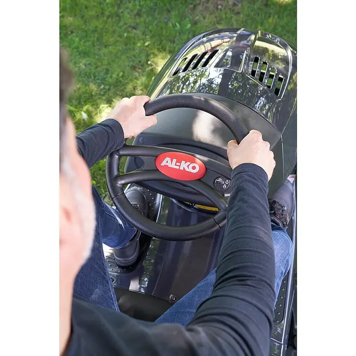 AL-KO Easy Rasentraktor 15-93.2 HDS-A - 452 cm³, Schnittbreite: 93 cm - Blick auf das AL-KO Aufsitzmäher-Cockpit mit Lenkrad, Bedienelementen und Fahrer in Jeans und dunklem Oberteil bei der Gartenarbeit.