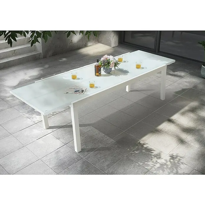 Mesa de jardín extensible Paris - L x An x Al: 180 x 90 x 75 cm, Aluminio/Vidrio, Blanco - Elegante imagen de una mesa de comedor blanca de exterior con tapa de cristal, decorada con bebidas, flores y un periódico.