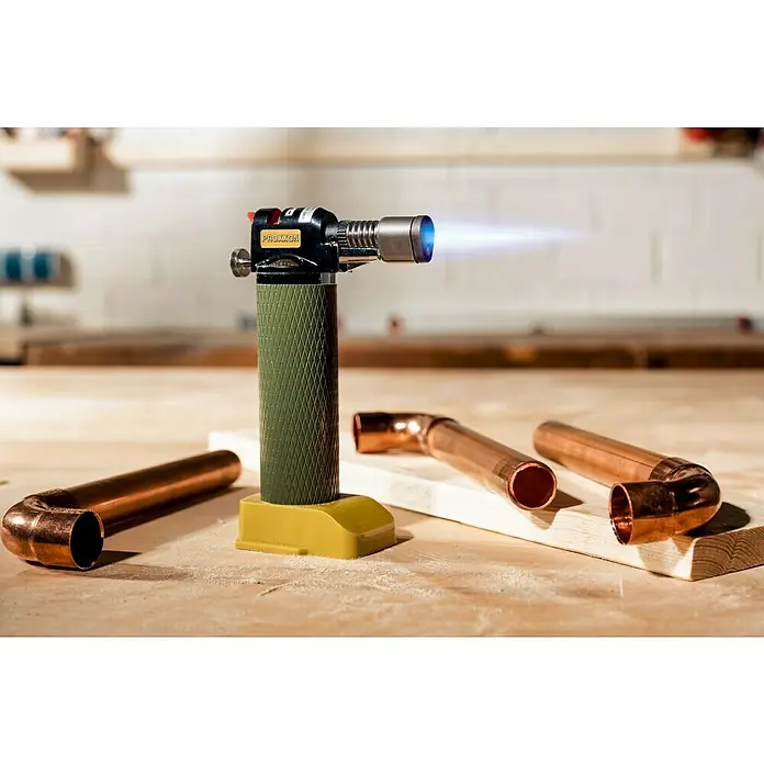 Proxxon Brenner Microflam MFB/E -  - Nahaufnahme eines Proxxon-Brenners mit blauer Flamme, umgeben von Kupferrohren auf einer Werkbank, ideal für Sanitärarbeiten.