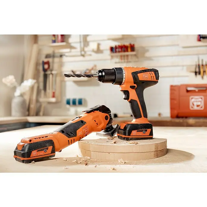 Fein Maschinen-Set Das Combo Kit Professionell AMM 300 Plus & ABSU 12 -  - Nahaufnahme eines FEIN Akku-Bohrschraubers und eines FEIN MultiMasters auf einem Holztisch mit Werkzeugen im Hintergrund.