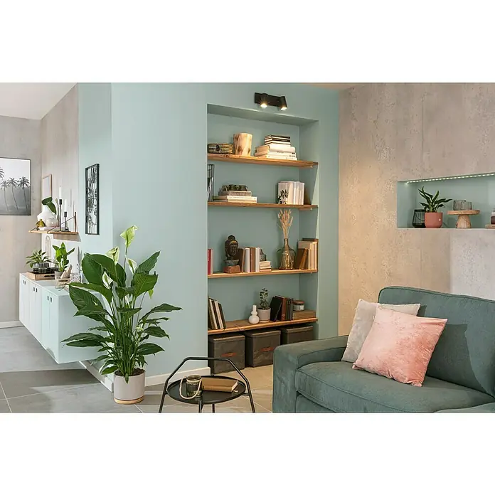 Piardino EinblattSpathiphyllum floribundum 'Lauretta', Topfgröße: 24 cm, Weiß - Ein elegantes Wohnzimmer mit einem Bücherregal in der Wand, das mit Büchern, Deko und Pflanzen gefüllt ist, neben einem grünen Sofa mit Kissen.