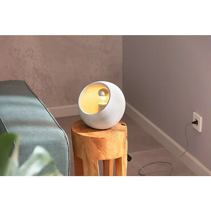 Paulmann Neordic Tischleuchte rund Ingram - 20 W, Ø x H: 230 mm x 21,5 cm, Grau, E27 - Eine moderne weiße Kugel-Tischlampe auf einem Holzhocker neben einem grauen Sofa, die ein warmes, einladendes Licht ausstrahlt.