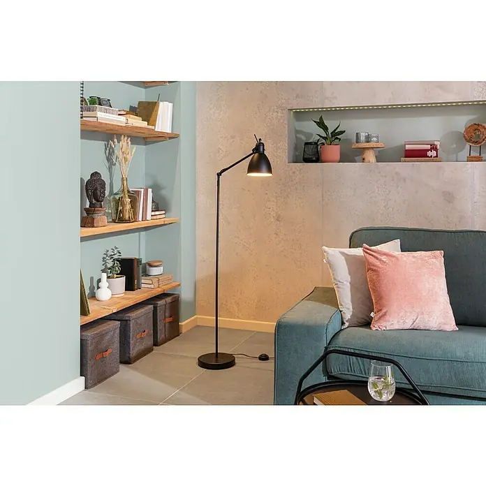 SCHÖNER WOHNEN-Farbe Naturell Wandfarbe KreidefarbeEukalyptuswald - kräftiges Blaugrün, Matt, 1 l, Konservierungsmittelfrei - Eine elegante schwarze Bogenlampe neben einem grünen Sofa, die eine warme und einladende Atmosphäre im Raum schafft. Bücherregal im Hintergrund.