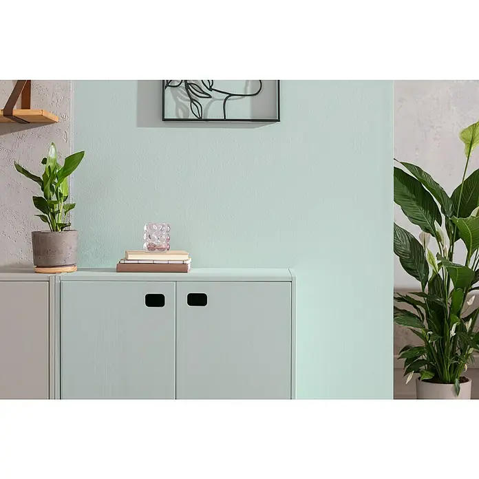 SCHÖNER WOHNEN-Farbe Naturell Wandfarbe KreidefarbeEukalyptuswald - kräftiges Blaugrün, Matt, 1 l, Konservierungsmittelfrei - Einrichtung mit einem mintgrünen Schrank mit Griffen, auf dem Bücher, eine Vase und eine Pflanze stehen, neben einer weiteren Pflanze.