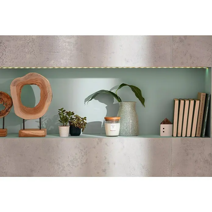 Vase Julia - Ø x H: 14 x 20 cm, Grün - Ein Regal mit Büchern, Pflanzen, einer Kerze und Holzdekoration, beleuchtet von einer LED-Leiste. Der Hintergrund ist hellblau.