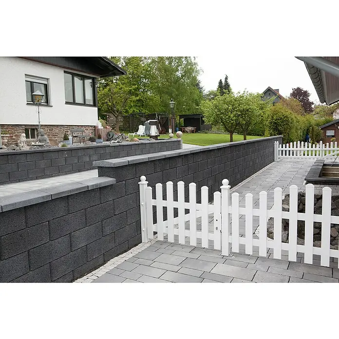 EHL Planomur Mauerstein Normalstein - Anthrazit, 50 x 25 x 20 cm, Beton - Eine weiße Gartenzaun-Pforte mit abgerundeten Spitzen und grauen Pflastersteinen, umgeben von grüner Vegetation.