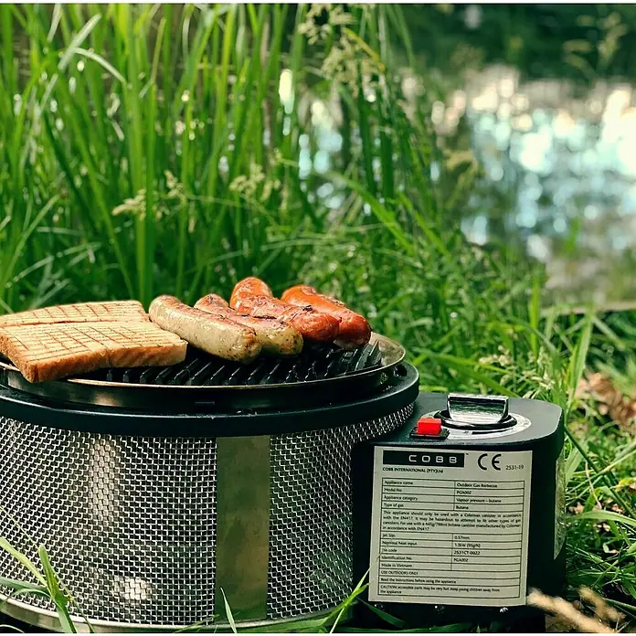 Cobb Gasgrill Deluxe - Durchmesser Grillfläche: 32 cm, 1,23 kW, Anzahl Brenner: 1 - Ein tragbarer COBB-Gasgrill mit Würstchen und Brot, ideal für Grillen im Freien.