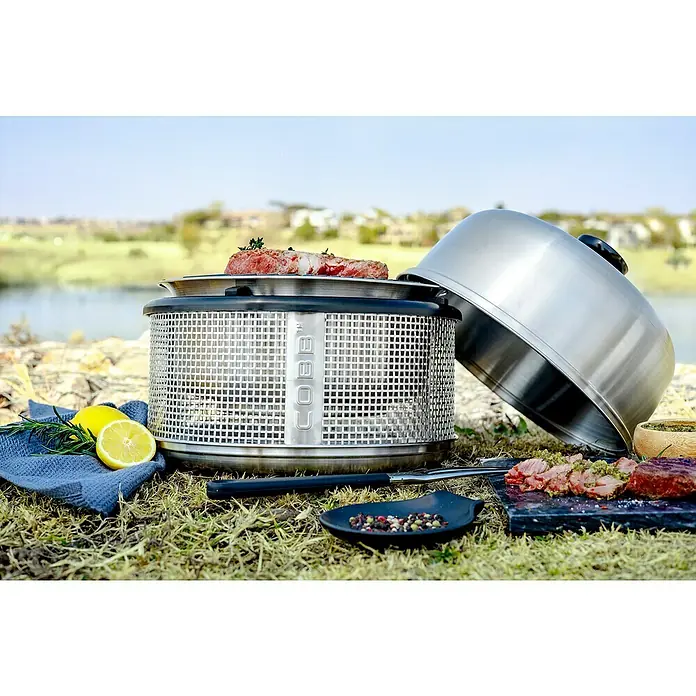 Cobb Holzkohlegrill Air DeluxeDurchmesser Grillfläche: 32 cm, Silber - Nahaufnahme eines Cobb-Grills im Freien mit Speisen.