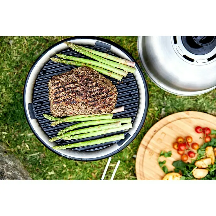 Cobb Holzkohlegrill Air DeluxeDurchmesser Grillfläche: 32 cm, Silber - Ein Grill mit Aspargel und Fleischstück, dazu eine Platte mit Gemüse. Perfekt für ein leckeres Outdoor-Essen mit Freunden.