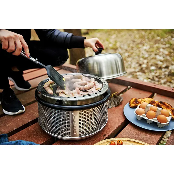 Cobb GrillpfanneDurchmesser: 30,4 cm, Höhe: 1,9 cm - Eine Person bereitet Speck und Wurst auf einem Cobb-Grill zu, mit Eiern und Toast als Beilage.