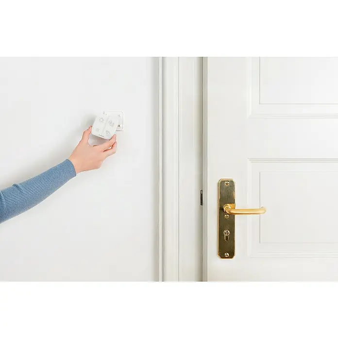 Bosch Smart Home Universalschalter II - Batteriebetrieben - Nahaufnahme einer Person, die einen Bosch Smart Home Controller an einer weißen Wand neben einer weißen Tür mit goldenem Griff montiert.