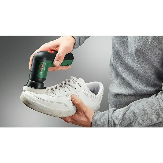 Bosch Akku-Reinigungsbürste UniversalBrush - 14 -tlg., 3,6 V, 2 Ah - Eine Person reinigt einen weißen Sneaker mit einer elektrischen Reinigungsbürste von Bosch, Modell UniversalBrush.