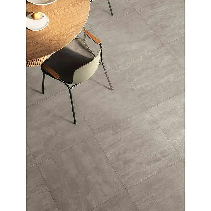 Atlas Concorde Solution Yorkshire Feinsteinzeugfliese Ash - 60 x 60 cm, Grau, Matt - Detailaufnahme von quadratischen Bodenfliesen in hellgrauer Farbe, die einen modernen Esstisch und Stuhl umgeben.