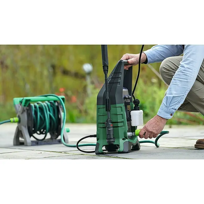 Bosch Universal Akku-Hochdruckreiniger UniversalAquatak 36V-100 - 8 -tlg., 36 V, 1 Akku - Ein grüner und schwarzer Hochdruckreiniger wird von einer Person mit einem Schlauch verbunden, mit einer Schlauchaufroller im Hintergrund.