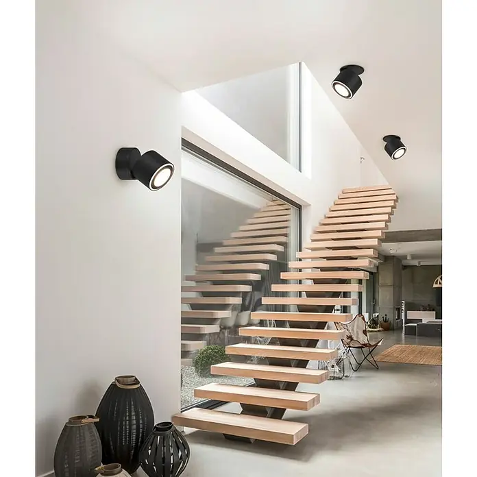 Trio Leuchten LED-Deckenstrahler Taurus - 5 W, Schwarz-matt, Warmweiß, 1 Stk. - Elegante Innenaufnahme mit schwebender Holztreppe und modernen schwarzen Strahlern, die ein stilvolles Ambiente schaffen.
