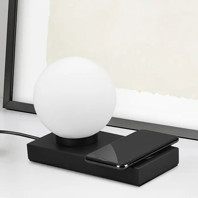 Reality Leuchten Tischleuchte Chloe - 40 W, L x B x H: 10 x 20 x 15 cm, Schwarz-matt, E14 - Diese Nahaufnahme zeigt eine Nachttischlampe mit einer kabellosen Ladestation für Mobiltelefone. Stilvolles Design für modernes Zuhause.