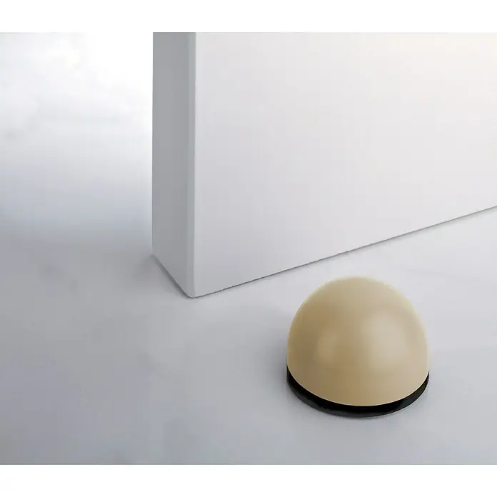 Inofix Tope de puerta 2033 - Oro, Plástico, 2 ud. - Primer plano de un tope de puerta en forma de cúpula con base negra, situado cerca de una pared blanca, mostrando estética minimalista.