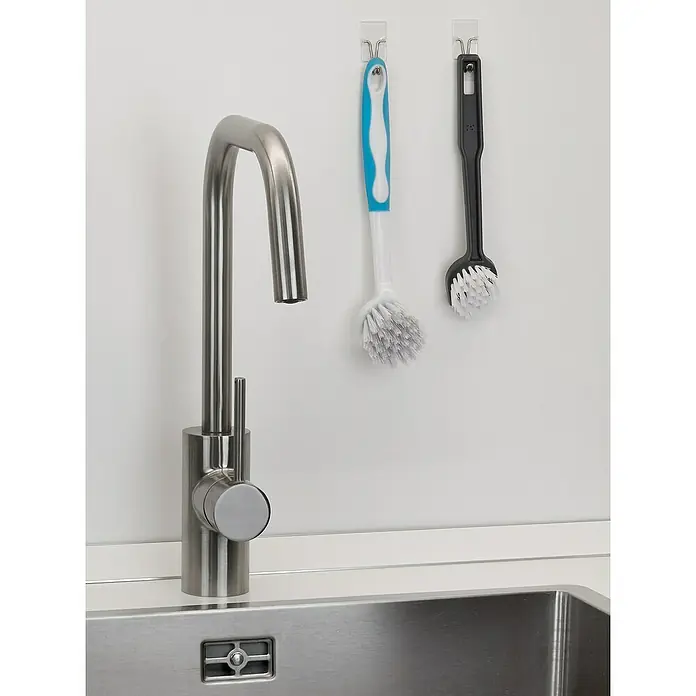 Inofix Gancho para colgar 2106 - Transparente, 2 ud. - Un moderno grifo de acero inoxidable junto a dos cepillos para platos colgados en una pared blanca, completando la instalación de la cocina.