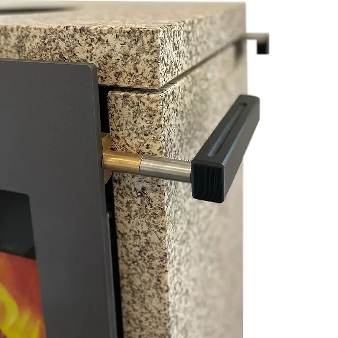 xeoos Kaminofen Patagonia X5 - 5 kW, Raumheizvermögen: 20 m³ - 70 m³, Farbe Verkleidung: Ming Yellow - Nahaufnahme eines Ofens mit Granitplatte und einem Griff aus Metall und Kunststoff. Das Design ist modern und robust.