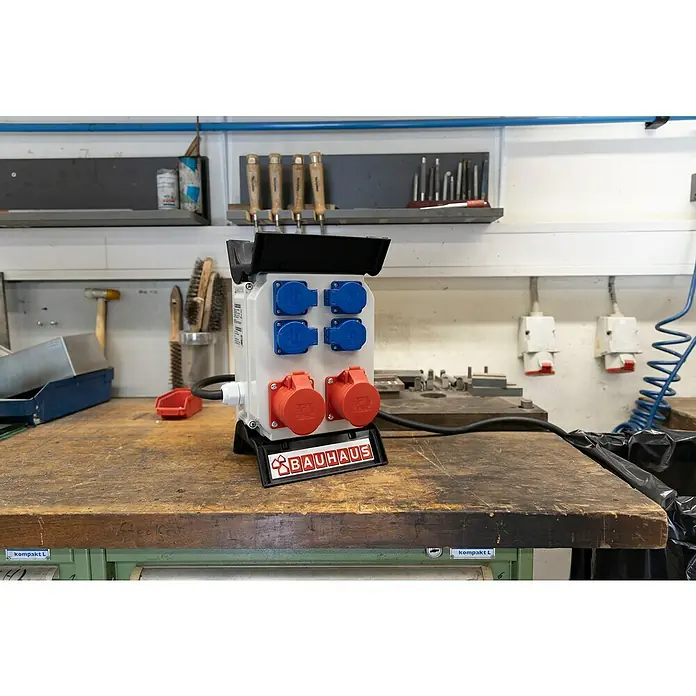 BAUHAUS Baustromverteiler - Anzahl CEE-Steckdosen: 2 Stk., Anzahl Steckdosen Schuko: 4 Stk., IP44 - Steckdosenverteiler von Bauhaus mit mehreren blauen und roten Anschlüssen auf einer Werkbank.