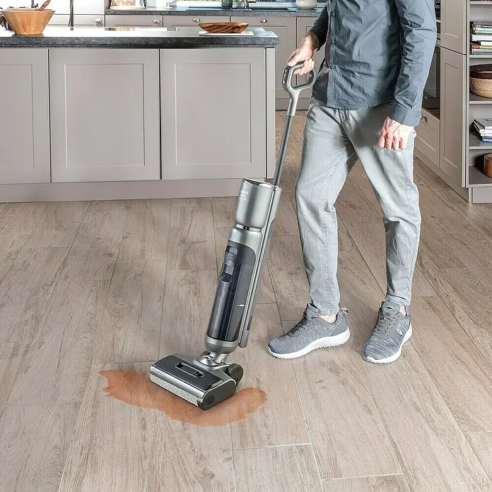 Thomas Akku-Hartbodenreiniger Aqua Floor Cleaner Cordless - 21,6 V - Mann reinigt verschüttete Flüssigkeit mit einem Nass-Trockensauger auf Holzboden. Der Sauger ist grau und schwarz.