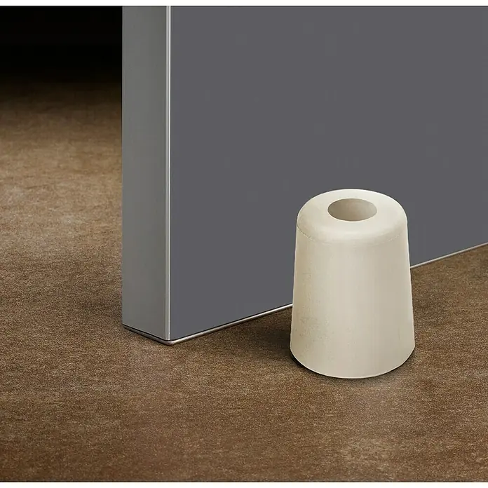 Inofix Tope de puerta 3048 - Caucho macizo, Marfil - Un tope de puerta blanco en forma de cono se encuentra al lado de una puerta gris, protegiendo el suelo y evitando portazos.