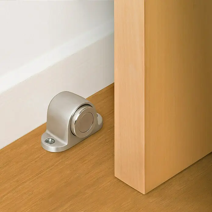 Inofix Tope de puerta 3166 - L x An x Al: 38 x 52 x 30 mm, Plata, Magnético - Primer plano de un tope magnético de puerta de metal conectado a una puerta de madera, mostrando su diseño elegante y funcionalidad.