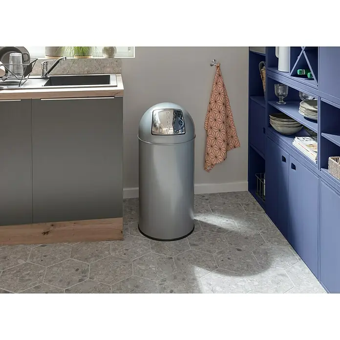 Vepa Bins Standard Mülleimer Pushcan - 40 l, Metall, Silber Metallic - Ein silberfarbener Treteimer aus Metall steht in einer Küche mit grauem Fußboden und blauem Schrank. Der Mülleimer hat einen glänzenden Deckel.