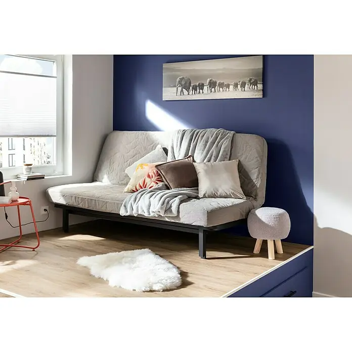 Decke Melange - Light Grey, 170 x 130 cm, 100 % Polyester - Helle Schlafcouch mit Kissen und Decken in einem gemütlichen Raum mit einem grauen Hocker und einem Bild von Elefanten.