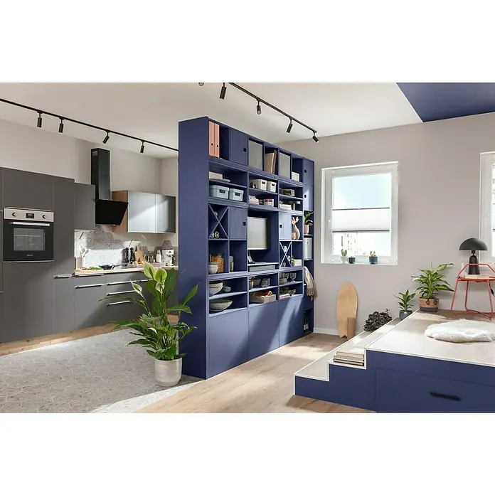 SCHÖNER WOHNEN-Farbe Wandfarbe Designfarbe - Sanftes Seidengrau, Matt, 2,5 l, Konservierungsmittelfrei - Offener Wohnraum mit grauer Küche und blauem Raumteiler-Regal, das als Bücherregal und Stauraum dient. Helle, moderne Einrichtung.