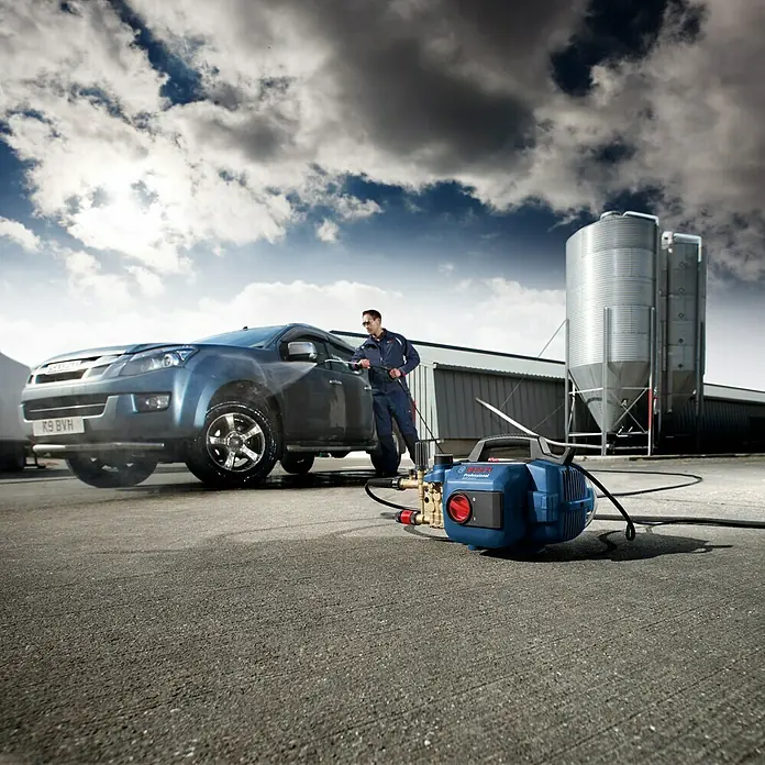 Bosch Professional Hochdruckreiniger GHP 5-13 C - 130 bar, 2.300 W, Fördermenge: 520 l/h - Der Bosch Hochdruckreiniger säubert ein Auto mit Kraft. Das blaue Gerät steht bereit für weitere Einsätze im Freien.