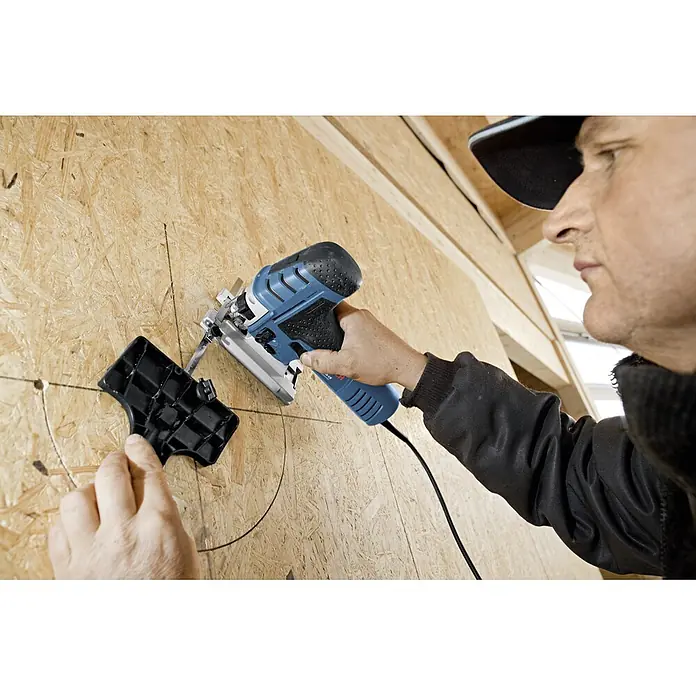 Bosch Professional Elektro-Pendelhubstichsäge GST 150 CE - 780 W, 500 /min - 3.100 /min, Anzahl Pendelhubstufen: 4 Stk. - Ein Handwerker verwendet eine Stichsäge, um ein Loch in eine Holzwand zu sägen, wobei er eine schwarze Führung verwendet.
