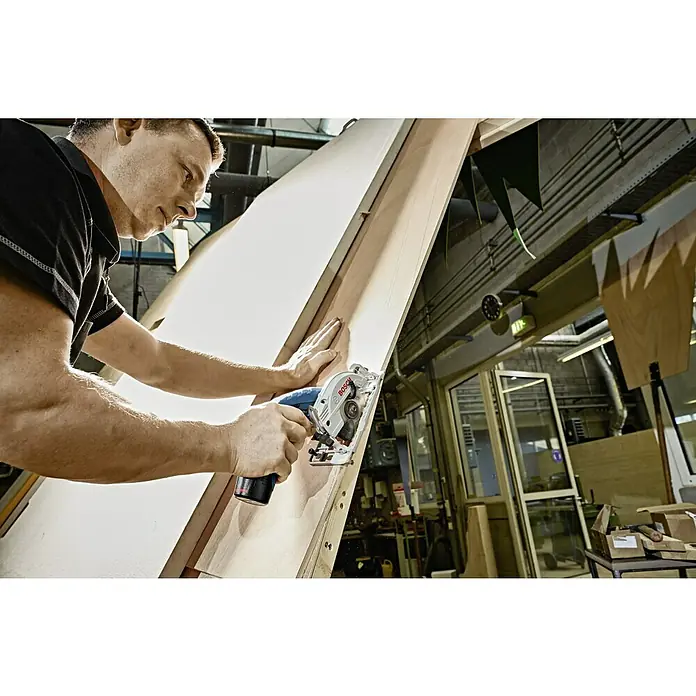 Bosch Professional Akku-Handkreissäge GKS 12V-26 - 12 V, Li-Ionen, Ohne Akku, Sägeblatt: 85 mm, 1.400 U/min - Ein Mann arbeitet mit einer Bosch-Kreissäge an einem Holzbrett in einer Werkstatt. Präzise Schnitte sind mit diesem Werkzeug einfach.