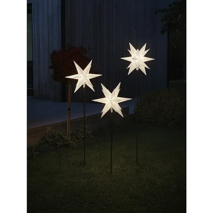 Konstsmide Standstern - Weiß, Warmweiß, LED, Netzbetrieben, 3 Stk. - Drei leuchtende Papierstern-Gartenstecker in einem Garten, die eine festliche und einladende Atmosphäre schaffen.