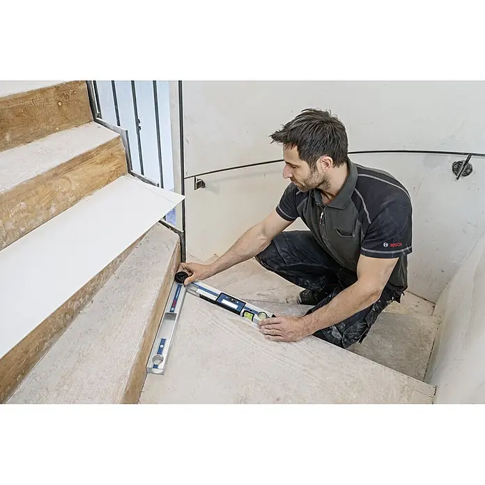 Bosch Professional Digitaler Winkelmesser GAM 220 - Messbereich: 0 - 220 ° - Mann misst mit einem Bosch Digital-Winkelmesser die Stufen einer Treppe, um genaue Winkel zu bestimmen.