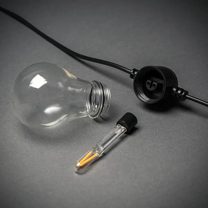 Konstsmide LED-Lichterkette - Außen, 4,5 cm, Bernstein, Oval, Solarbetrieben - Nahaufnahme einer zerlegten Glühbirnen-Lichterkette mit klarem Glaskolben, LED-Filament und Lampenfassung auf grauem Untergrund.
