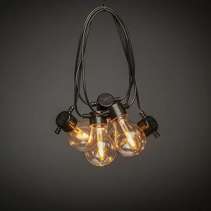 Konstsmide LED-Lichterkette - Außen, 4,5 cm, Bernstein, Oval, Solarbetrieben - Nahaufnahme einer dekorativen Lichterkette mit warm leuchtenden Glühbirnen und schwarzen Fassungen vor einem dunklen Hintergrund.