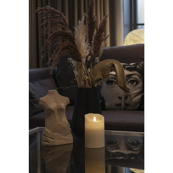 Konstsmide LED-Kerze - Beige, Wachs, 8,8 x 13,4 cm - Nahaufnahme eines Tisches mit Dekorationen: Eine Skulptur, eine Kerze und eine Vase mit getrockneten Blumen schaffen eine ruhige Atmosphäre.