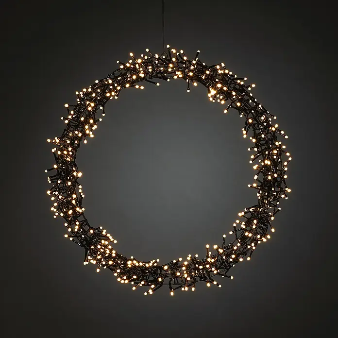 Konstsmide LED-KranzDurchmesser: 50 cm, Bernstein - Ein kreisförmiger Lichterkranz mit warmweißen Lichtern hängt vor einem dunklen Hintergrund und sorgt für eine festliche Atmosphäre.