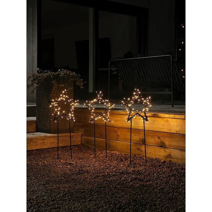 Konstsmide LED-Gartenstecker Stern 3er-SetSchwarz, Bernstein, Außen, 3 Stk. - Drei leuchtende Stern-Gartenstecker auf Kies vor einer Terrasse. Die Sterne sorgen für eine festliche Atmosphäre im Außenbereich.