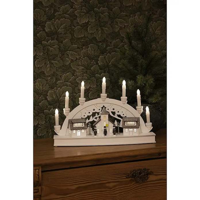 Konstsmide LED-Holzsilhouette Häuser - 10 x 43 x 28 cm, Weiß, Batteriebetrieben, Warmweiß - Weihnachtliche Fensterbeleuchtung mit sieben Kerzen und einer Szene mit Häusern und Figuren, die eine warme, festliche Atmosphäre schafft.