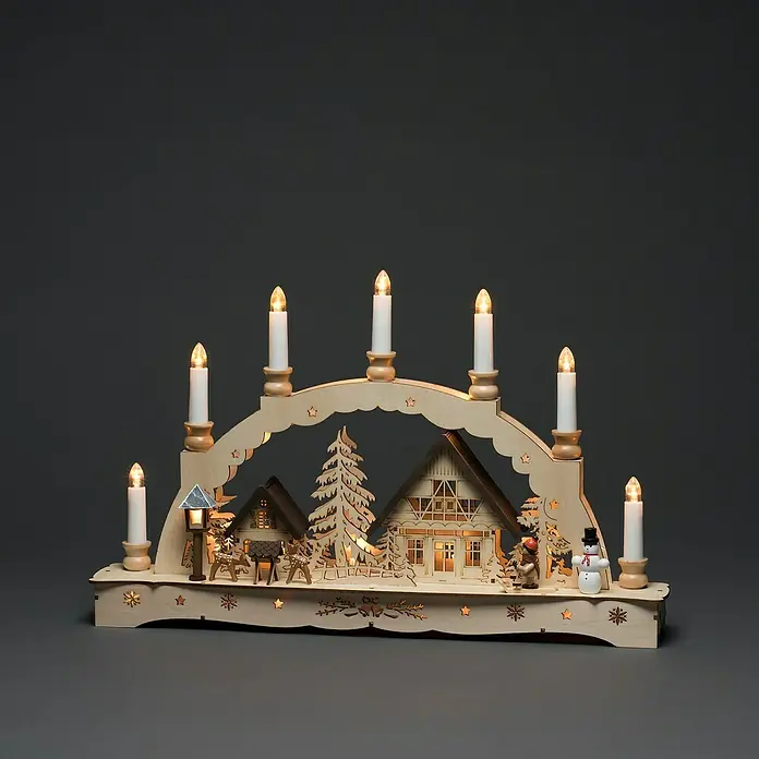 Konstsmide LED-Lichterbogen - Batteriebetrieben, L x B x H: 48 x 8 x 30 cm, Warmweiß, Naturfarben - Dekorative Lichterbogen-Szene mit Holzhäusern, Tannenbaum, Rentieren und Schneemann unter sieben Kerzen, die eine warme, festliche Atmosphäre schaffen.
