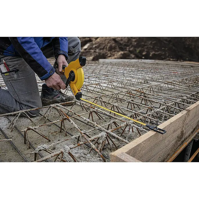 Stabila Rahmenmaßband 50 m - 50 m, Genauigkeitsklasse: II, Material: Stahlband - Nahaufnahme eines gelben Stabila Rollbandmaßes bei der Messung von Stahlbewehrung auf einer Baustelle, das die Präzision des Werkzeugs hervorhebt.