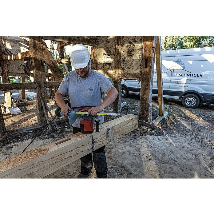 Stabila Zollstock - 2 m - Ein Zimmermann arbeitet an einem Holzbalken mit einer Hilti-Bohrmaschine, um präzise Löcher zu erstellen, während er einen Schutzhelm trägt.